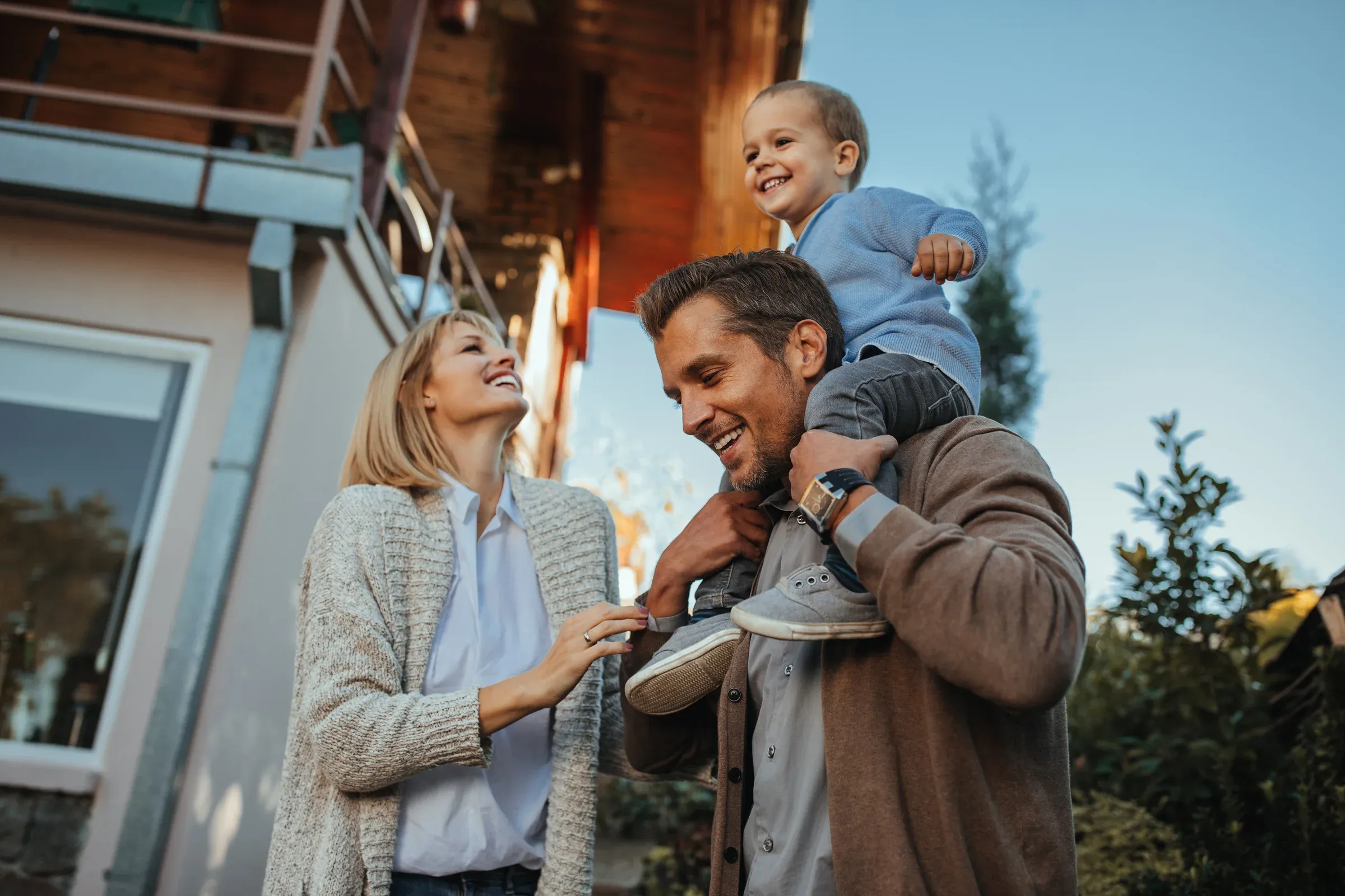 Lachende Familie mit Kleinkind vor einem modernen Wohnhaus
