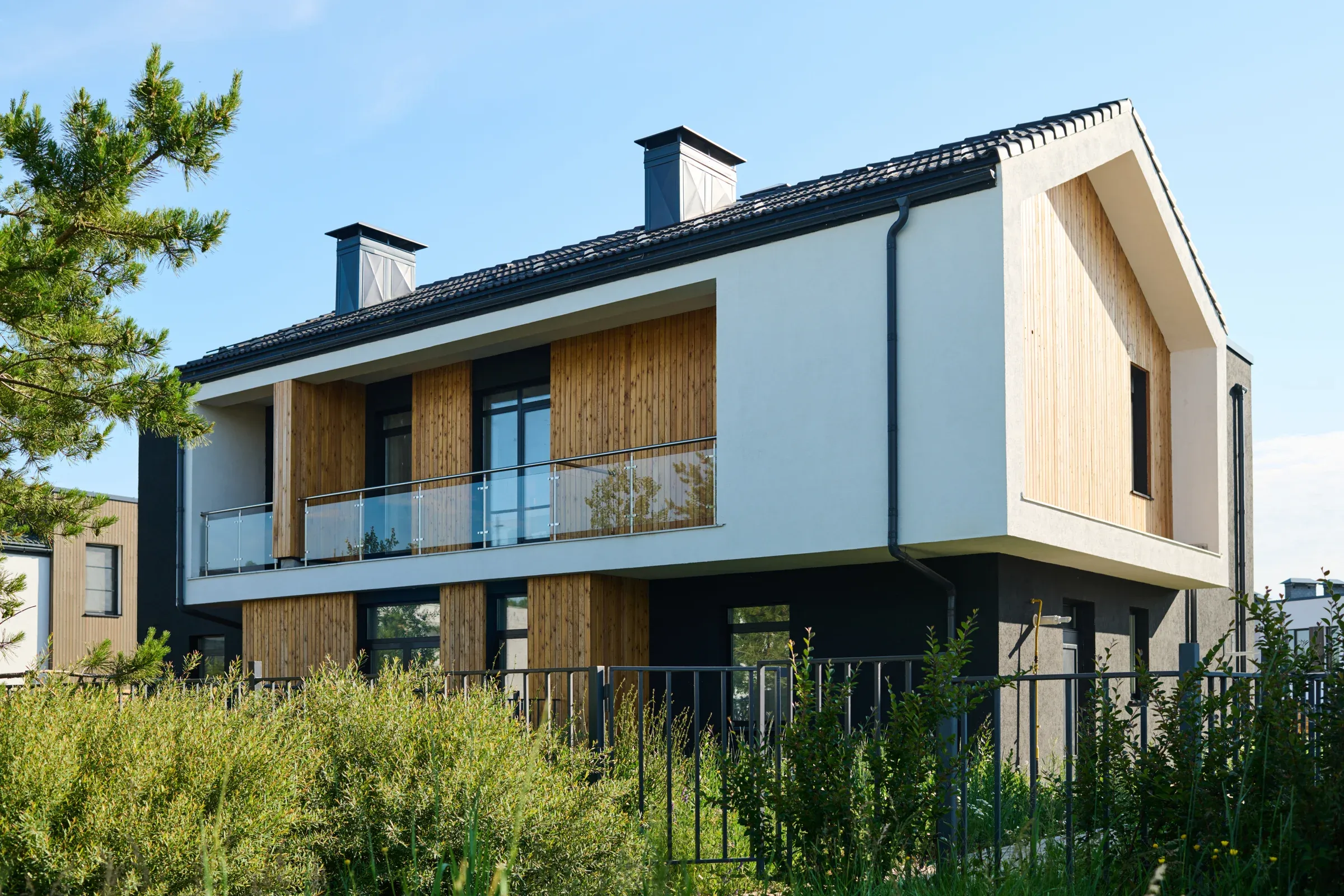 Modernes Wohnhaus mit Holzfassade und Balkon in einem grünen Garten